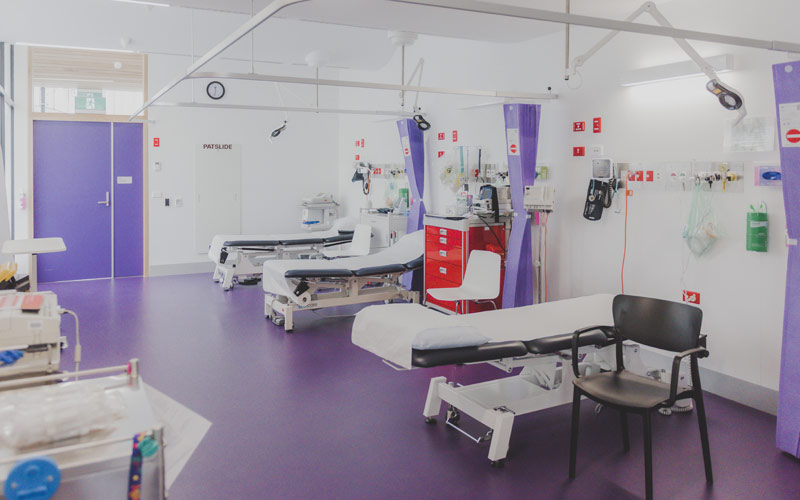 Photo of medial treatment room with beds and purple floor, door and curtains