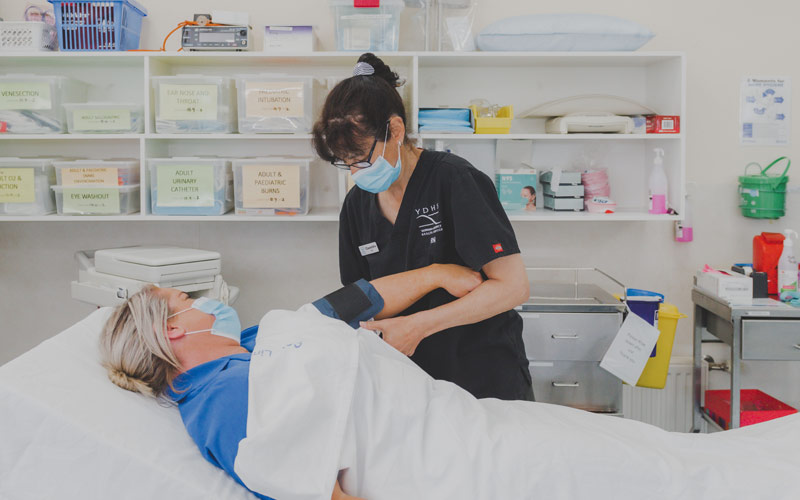Photo of a nurse wearing black tending to a female patient lying in a hospital bed