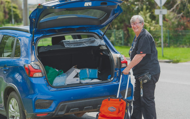 Photo of a female travelling nurse loading equipment into the boot of a blue car