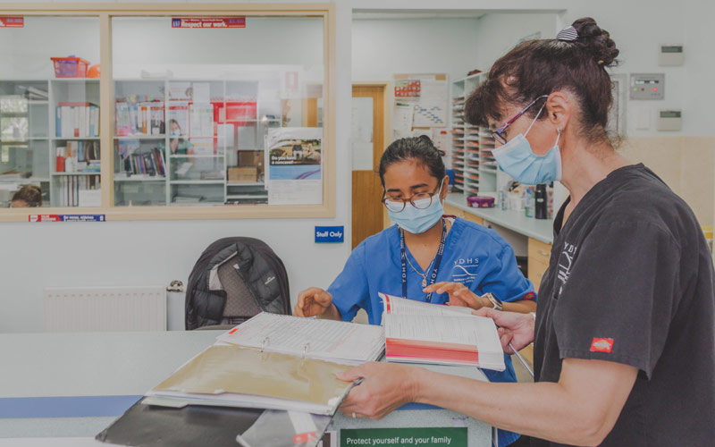 Photo of two female nurses looking at books and folders of information