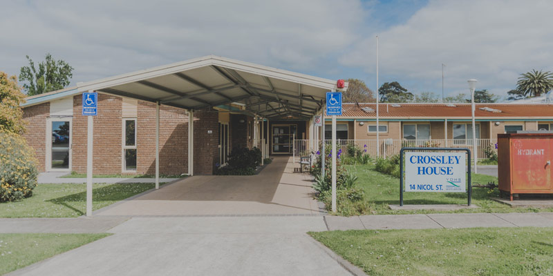 Photo of the entry to Crossley House Hostel with driveway and covered walkway in the foreground, brown brick building in the background.